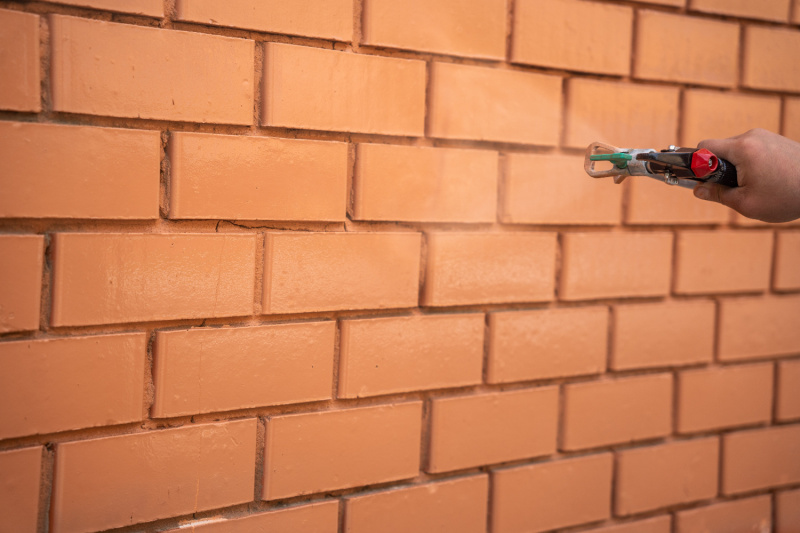 Painter using a professional spray gun to apply smooth, even paint coverage on a brick wall in Charlotte, North Carolina.