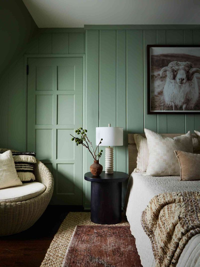 Muted Greens and Calm Naturals for a Fresh, Timeless Bedroom Bedroom with muted green paneled walls, soft neutral bedding, woven chair, and layered natural textures in a calm spring palette.